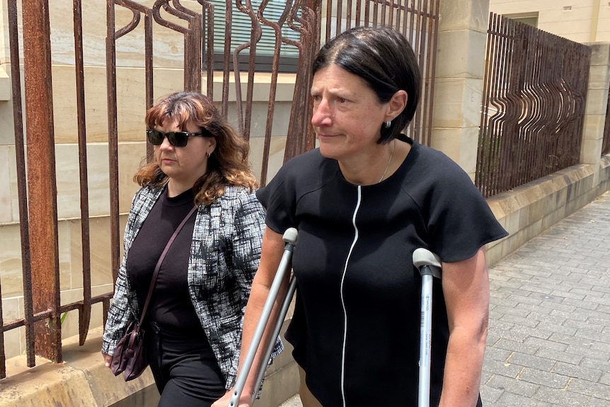 Two women walk along a fence outside a court building, one is on crutches