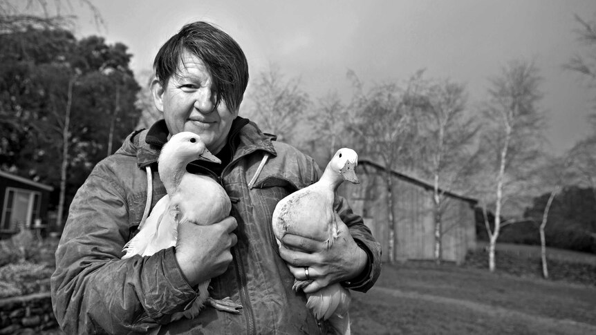 A black and white photo of Annie Smithers shows her in a field while holding two white ducks.
