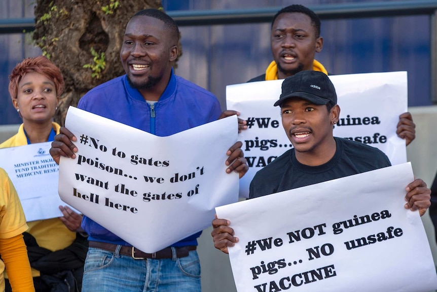 People hold up signs saying things like: "We not guinea pigs... No unsafe vaccine."