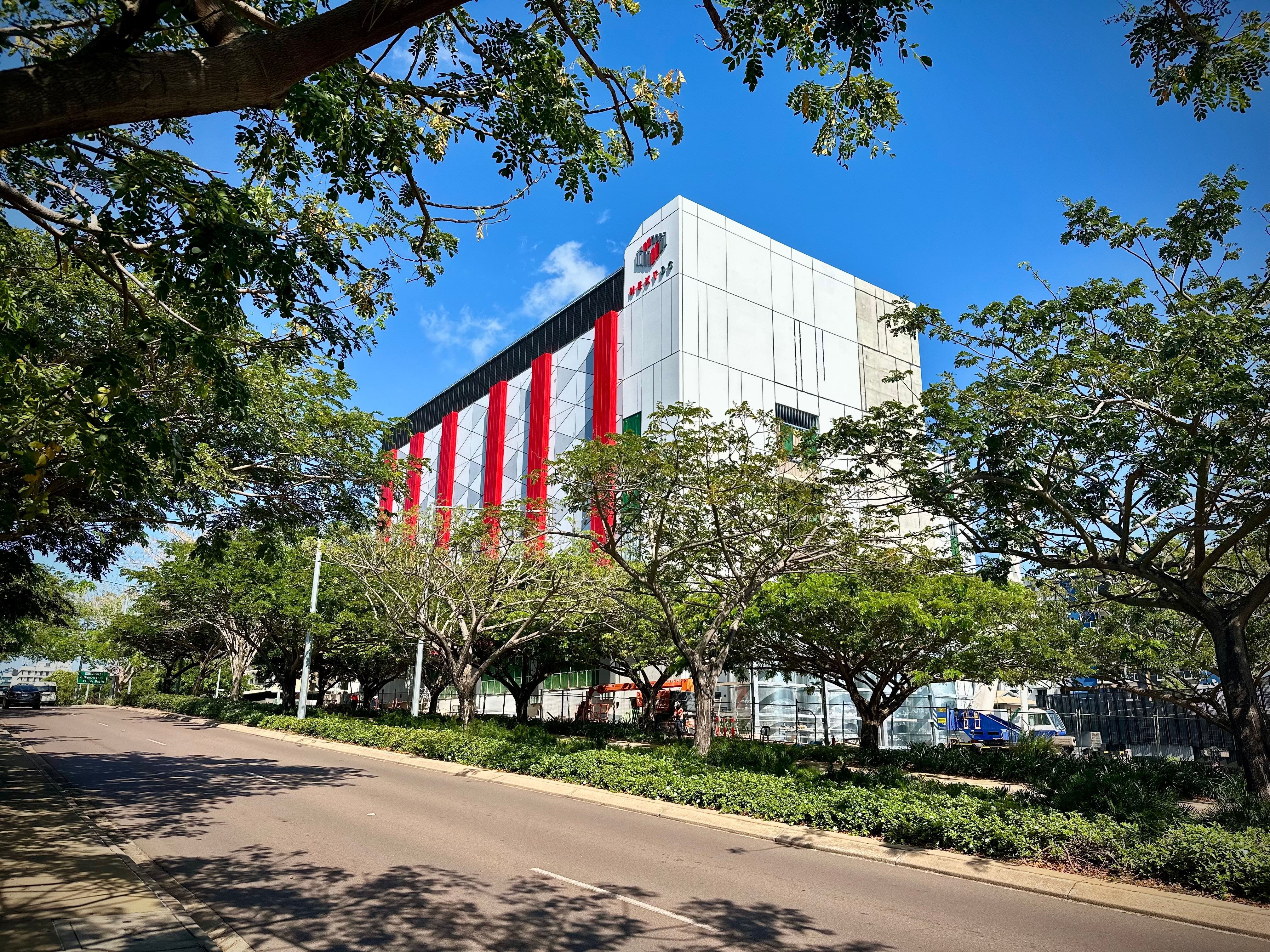 A large building with grey and red cladding on a tree-lined street.