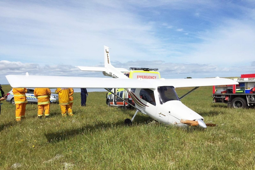 Emergency services parked next to a light plane in a paddock