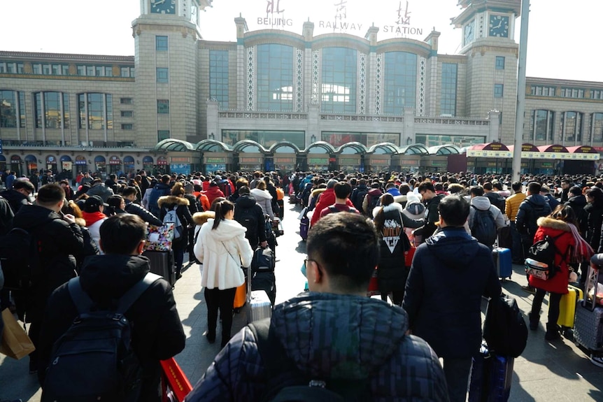 A number of people line up outside the Beijing Railway Station building.