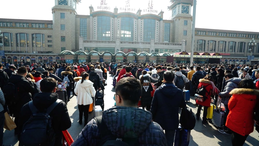 A number of people line up outside the Beijing Railway Station building.