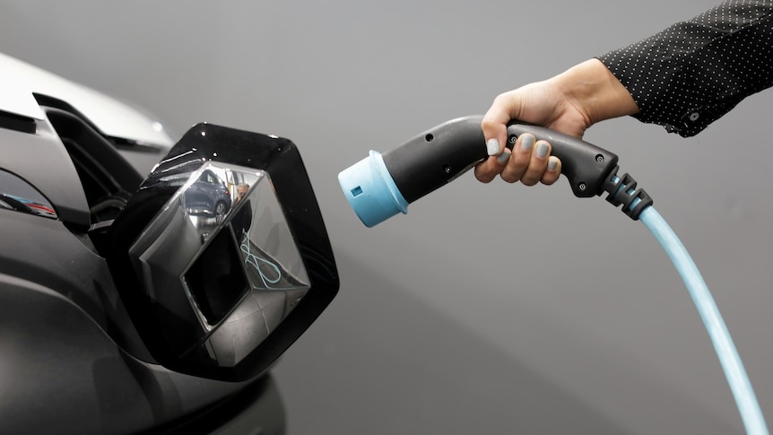 A woman holds a cable to charge an electric vehicle.