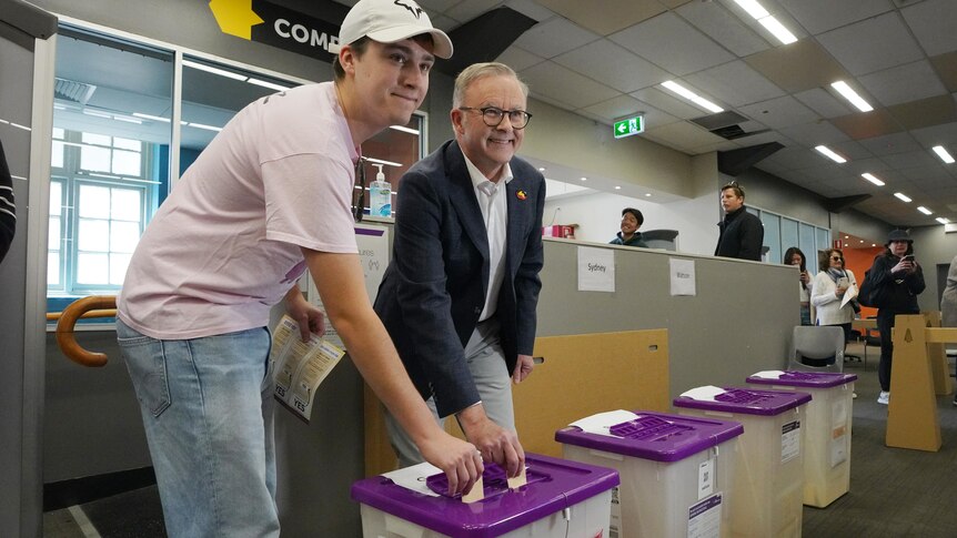 Two men put ballot papers into a box.
