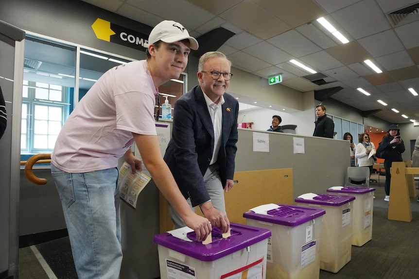 Two men put ballot papers into a box.
