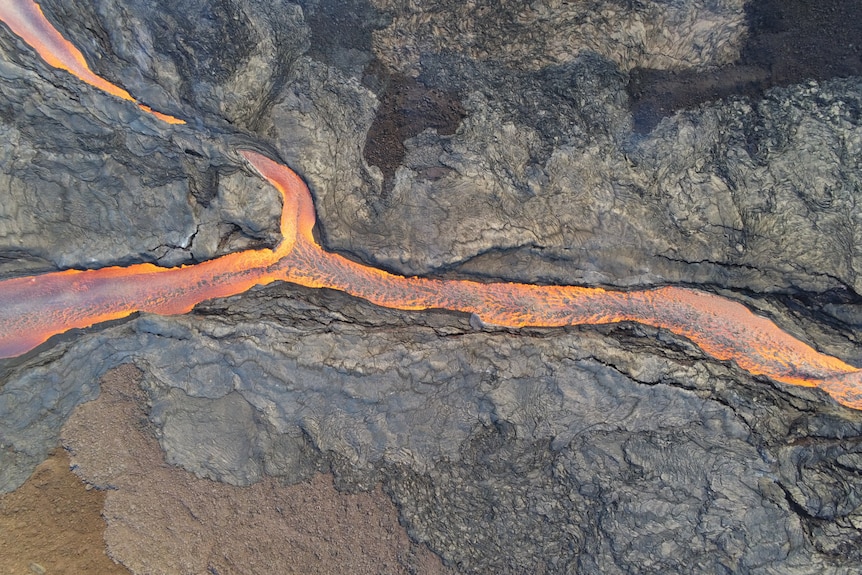 An aerial image of a lava channel with a rocky barren environment and red glowing lava.