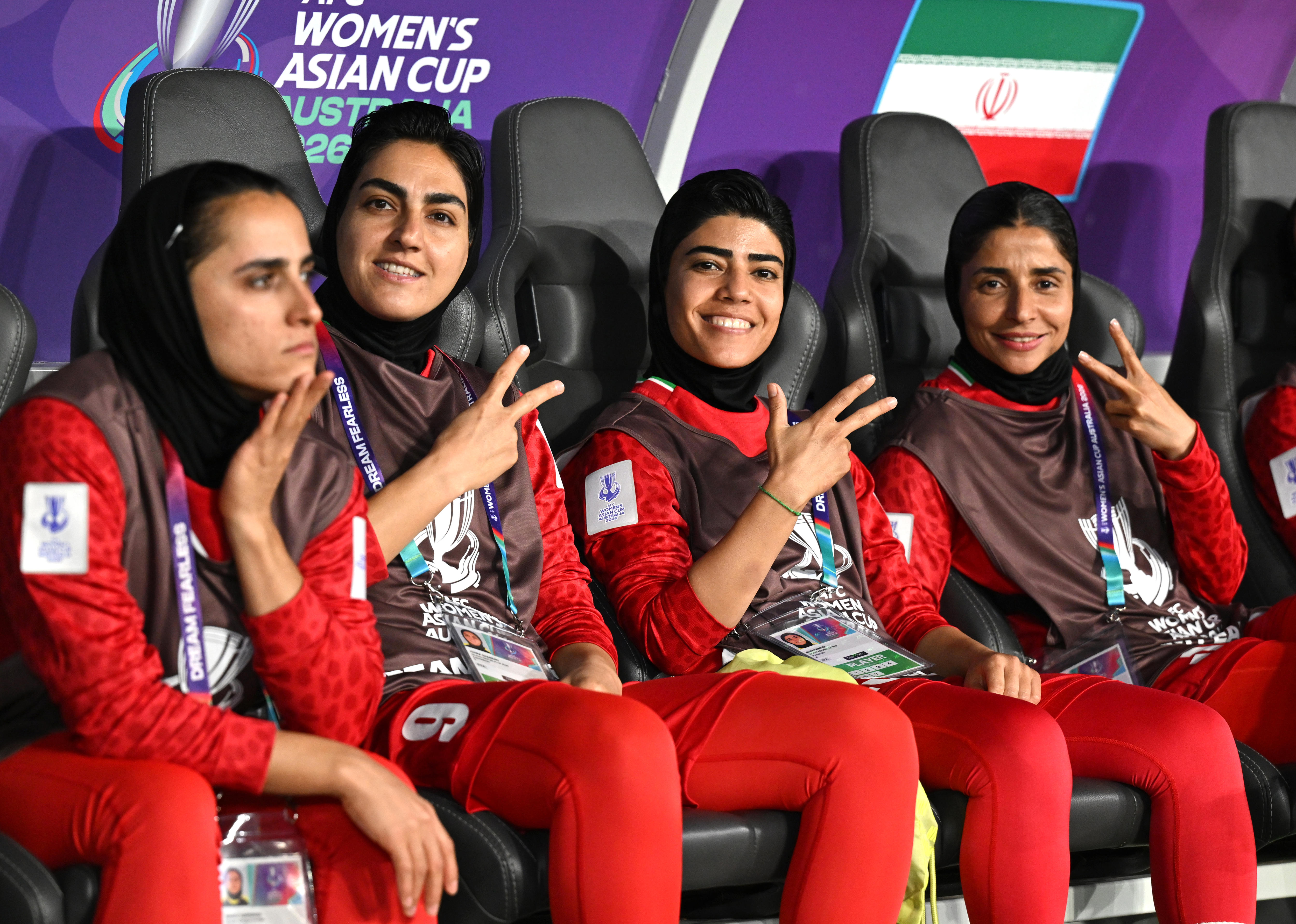 Members of the Iran women's football team flash peace signs as they sit on the bench