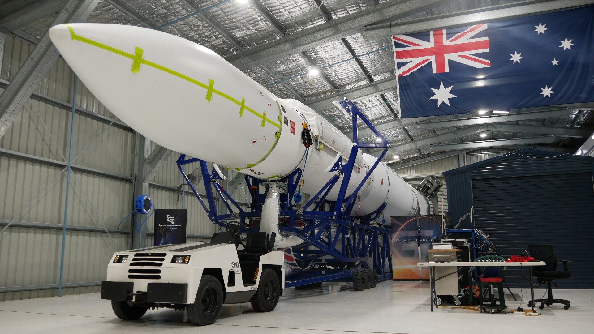 Rocket sits in warehouse on the back of small motorised vehicle.