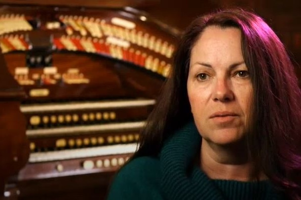 A dark-haired woman sits in front of an organ.