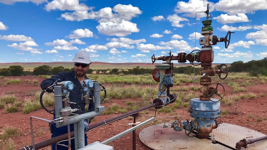 Man standing behind gas well checking valve.