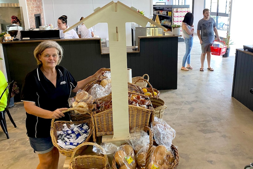 A woman stands beside a table piled with bread and packets of food.