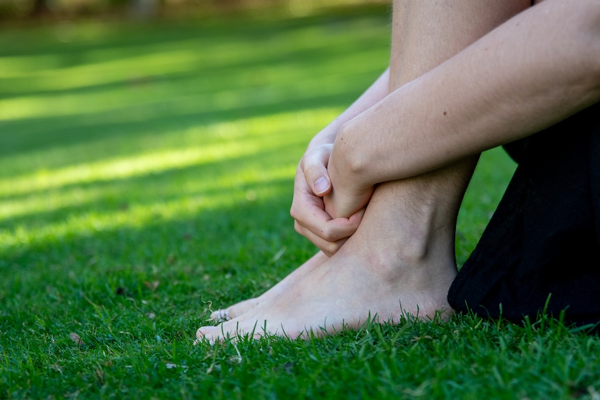 Woman's hands clasped over feet as she sits on grass