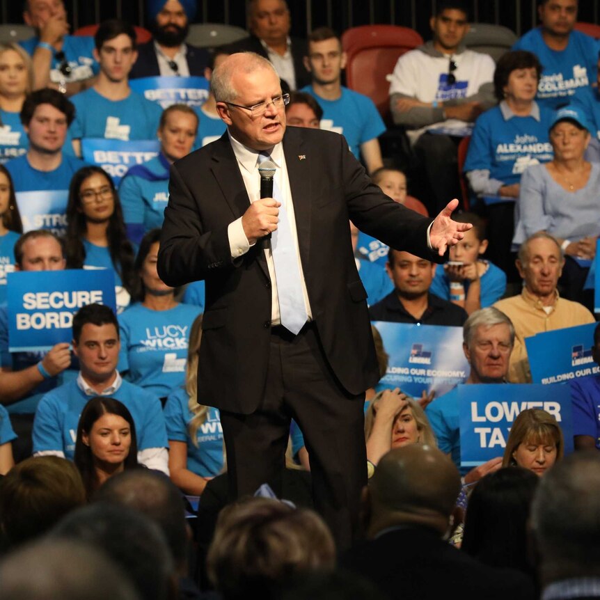 Scott Morrison stands on a stage holding a mic surrounded by supporters