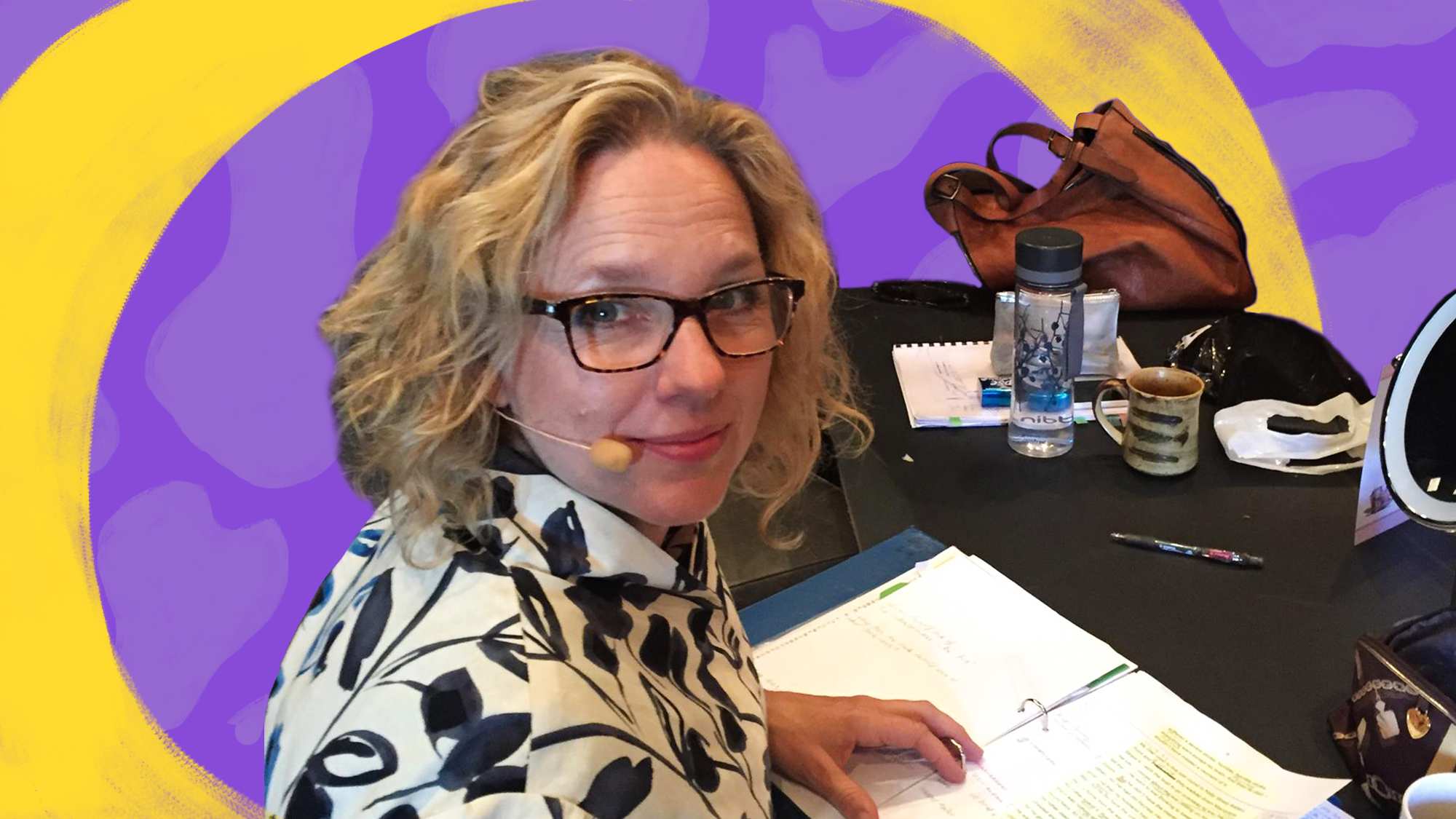 Jane at a desk with a document in front of her. She's turned to look at the camera and is wearing a small microphone on her head