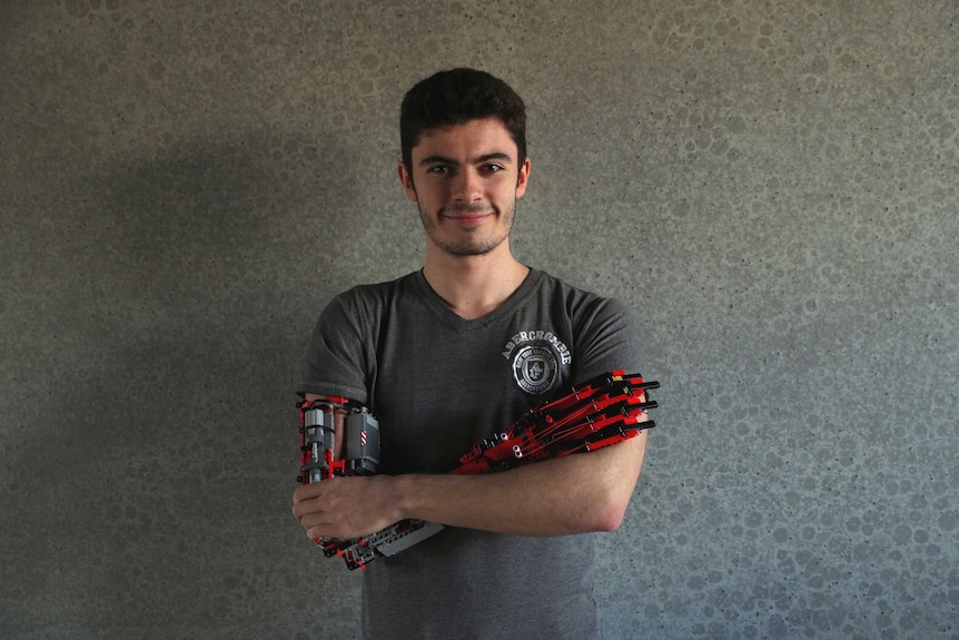 David Aguilar, wearing a prosthetic right arm made of Lego, crosses his arms.