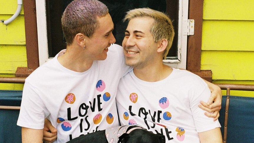 Two men wearing matching t-shirts with the words "love is love" across the front sit with a dog.