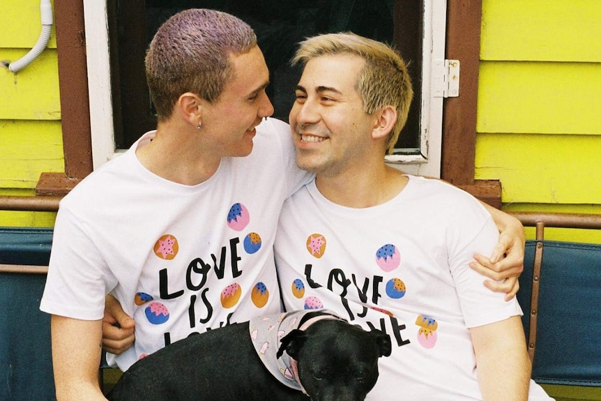 Two men wearing matching t-shirts with the words "love is love" across the front sit with a dog.