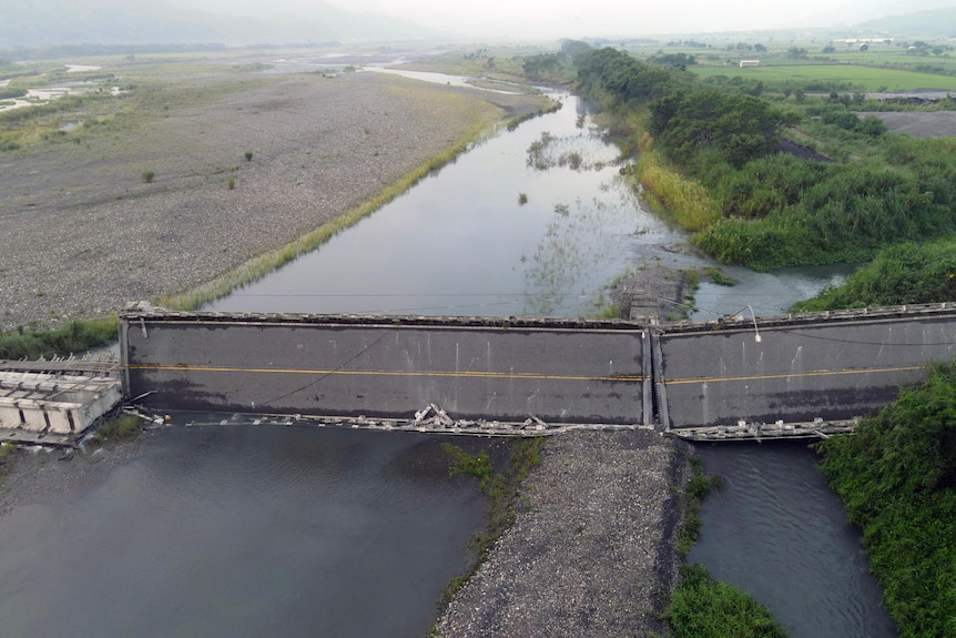 Drone photo of a bridge over a river, where most of it has fallen onto its side. 