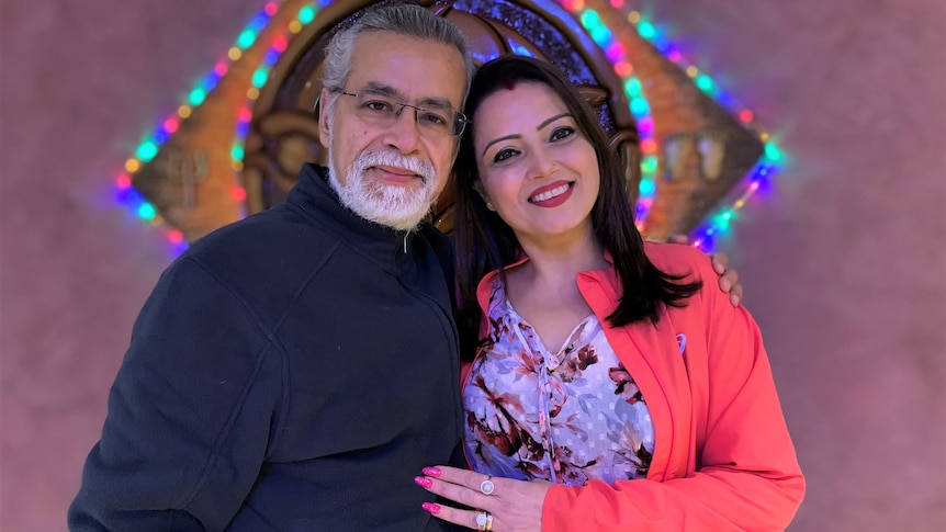 A man and a woman cuddle in front of some sparkly lights at their home