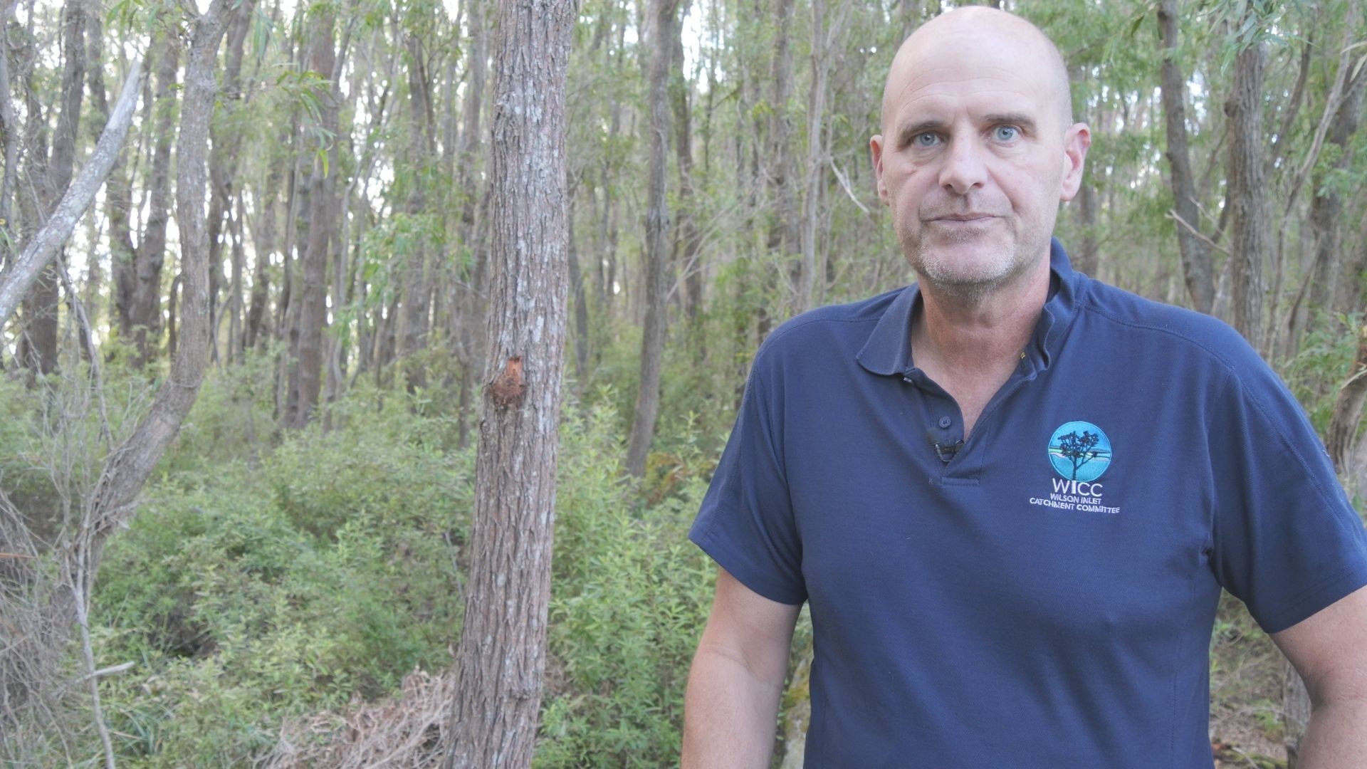 Shaun Ossinger wears a blue t-shirt, trees in the background.