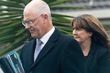 A man and a woman walk towards a car, holding binders and folders under their arms.