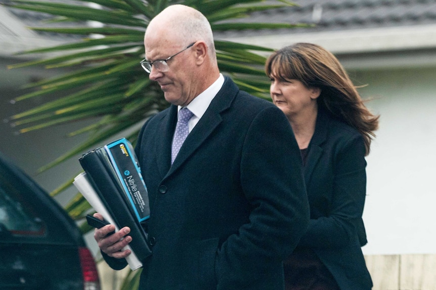 A man and a woman walk towards a car, holding binders and folders under their arms.