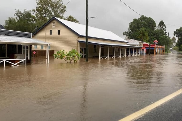 Murky brown water flloods a line of houses and shops in a regional town on a grey overcast day