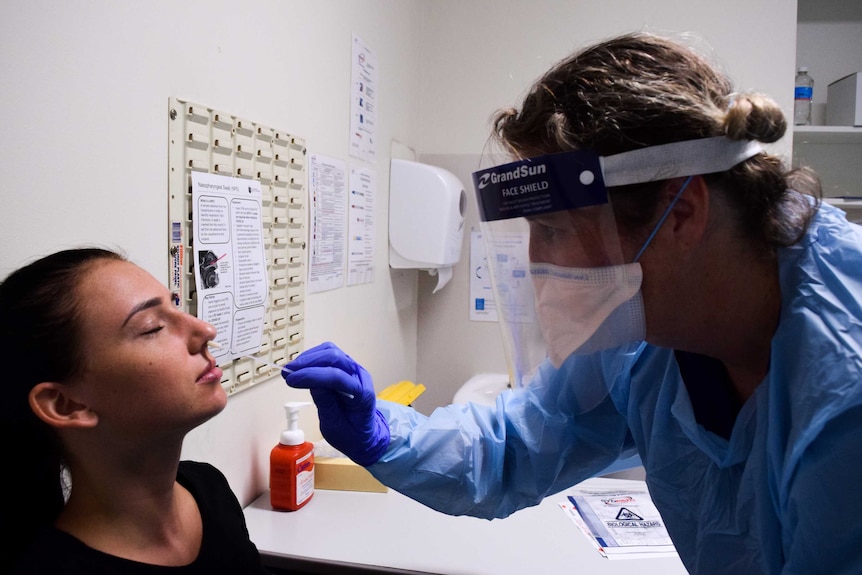 a woman being swabbed a clinic worker in full medical protective gear