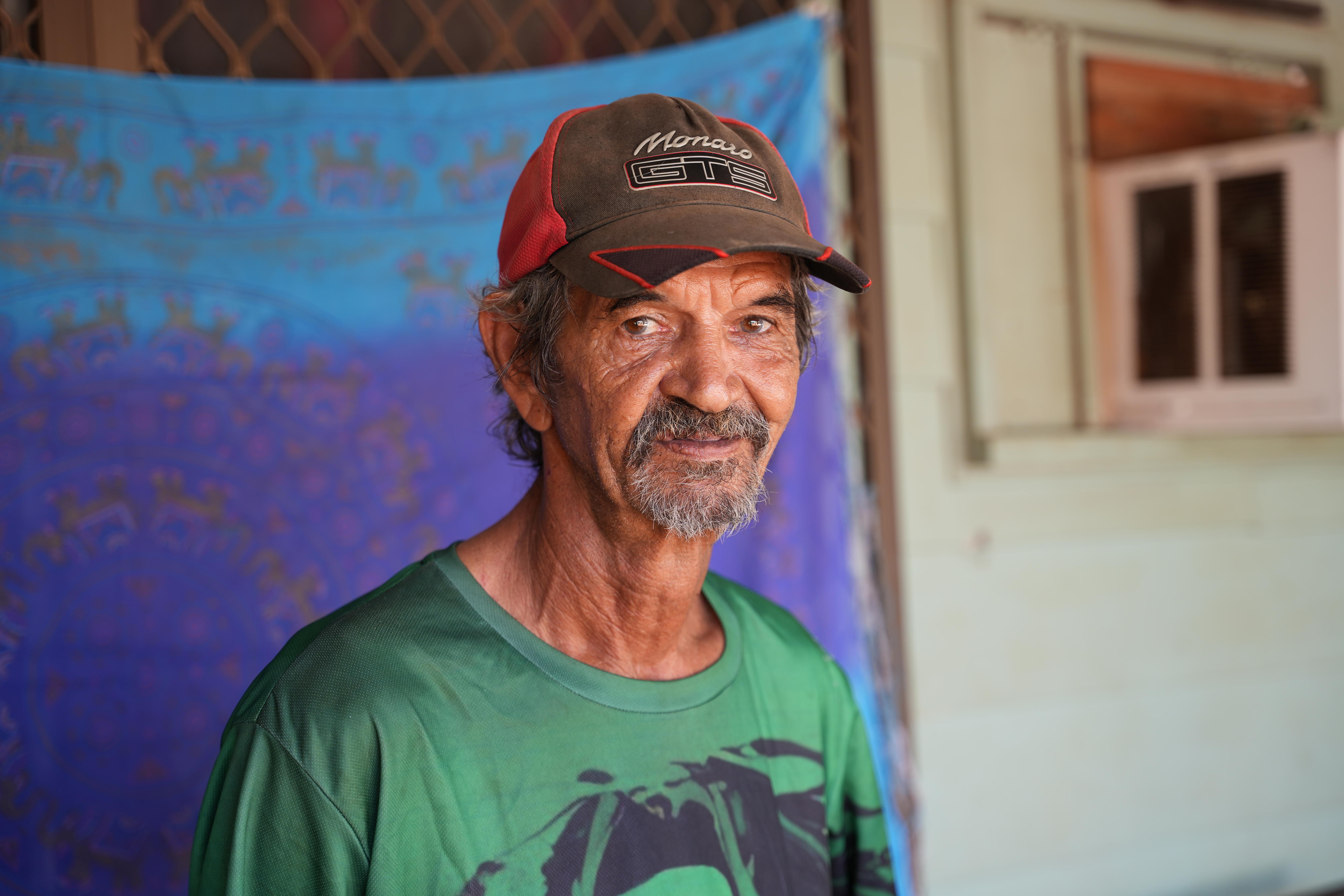 A man in a baseball cap and green t shirt looks at the camera
