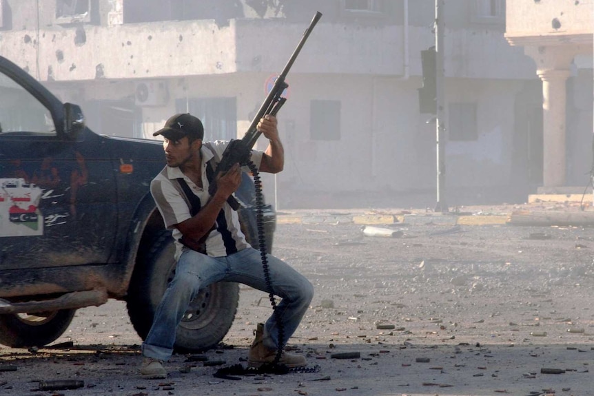 A Libyan fighter holds a gun behind a car.