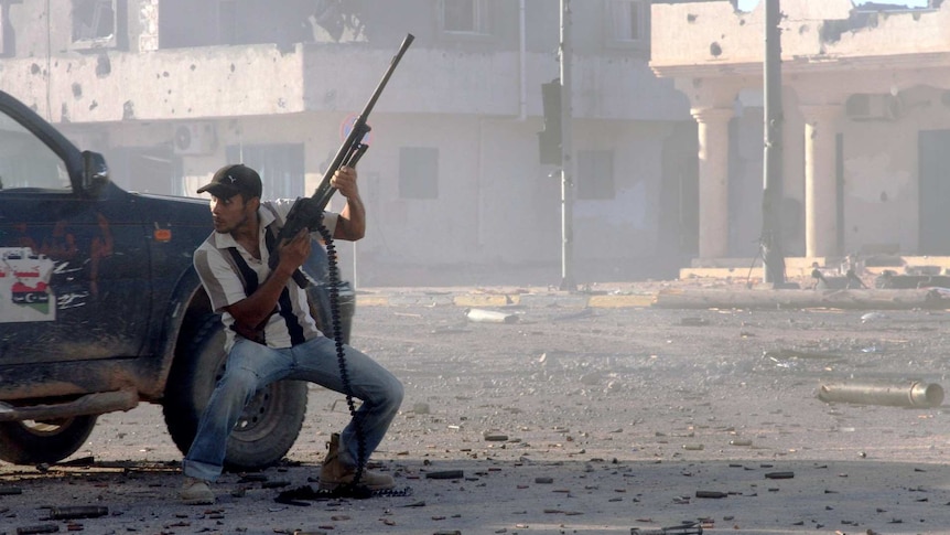 A Libyan fighter holds a gun behind a car.