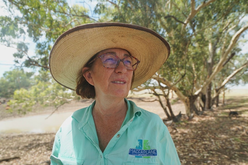 A woman wearing a green shirt and wide brimmed hat looks into the distance