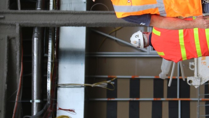 A man in a high-bis vest and white hardhat walking on a construction site.