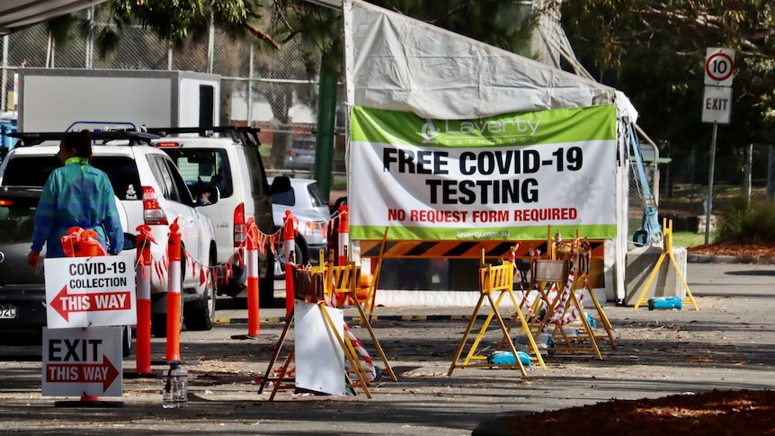 A drive-through testing site for COVID-19 with cars where a sign says that tests are screened by Laverty.