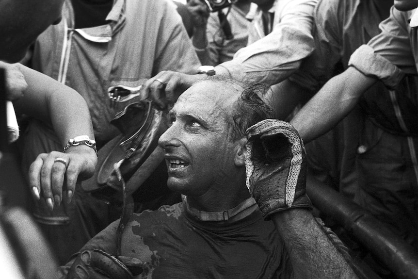 Black and white photo of a Formula 1 driver in his car in 1957.