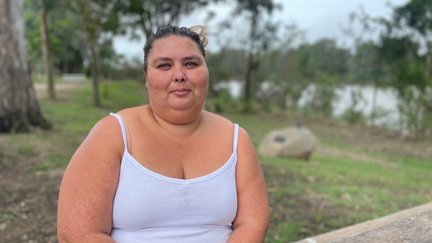 A woman sits at a park bench next to a rive and smiles 