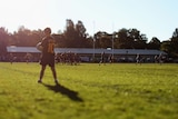 A young boy in a rugby jersey stands on the sidelines of a rugby game