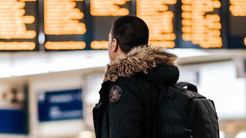 A man looks at flights in an airport, for a story about travel insurance and the novel coronavirus.