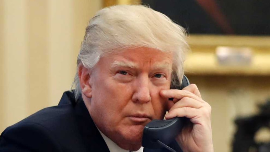 Donald Trump speaks on the phone at his desk in the Oval Office