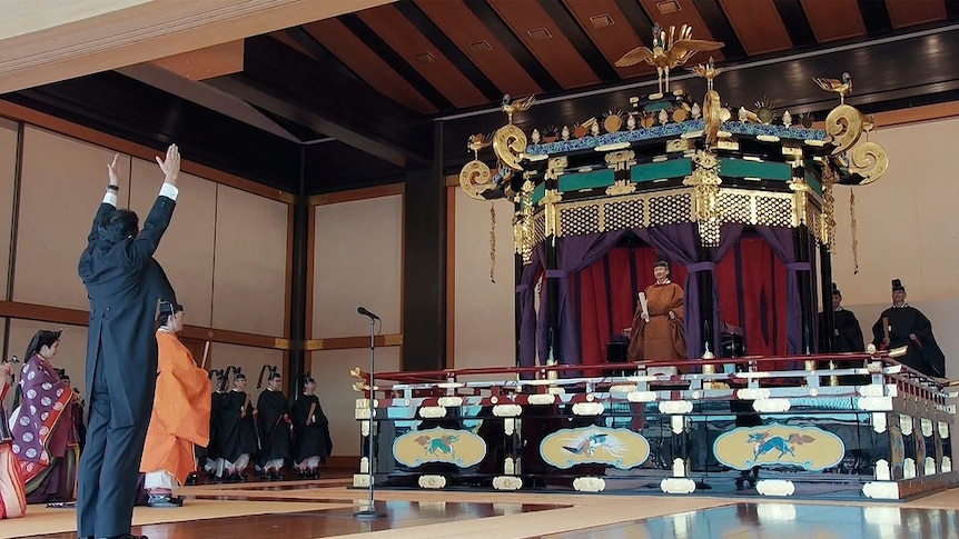 Prime Minister Shinzo Abe rising his hands at the emperor on a throne.