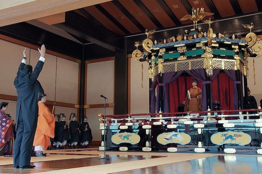 Prime Minister Shinzo Abe rising his hands at the emperor on a throne.