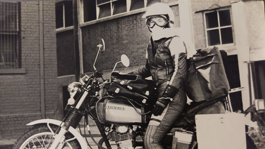 A woman on a motorbike, dressed in riding leathers.