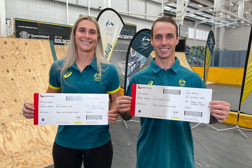 A man and a woman in green and gold jerseys stand holding over-sized plane tickets