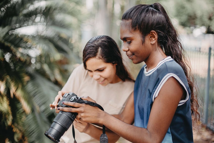 Two young Indigenous girls looking at photos on a camera