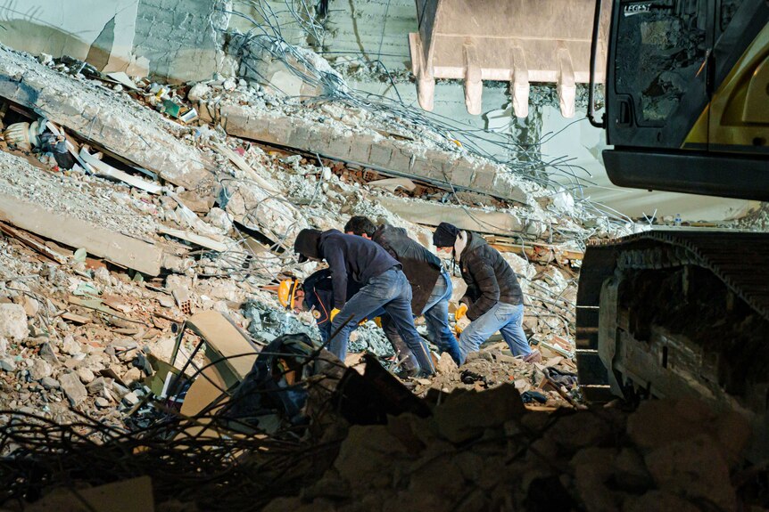 Men in hoodies bent over rubble 