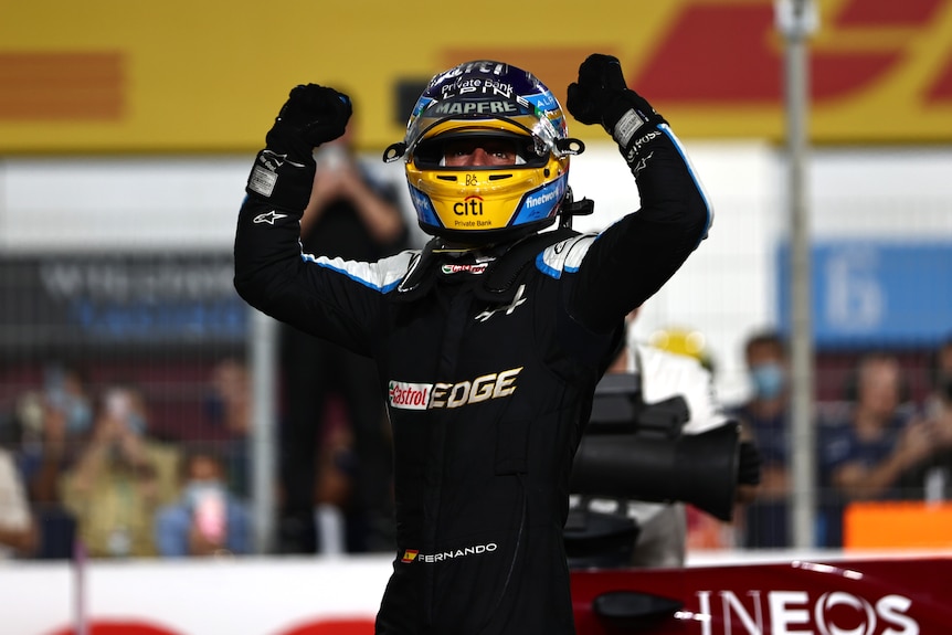 Racing driver raises his arms in celebration. 