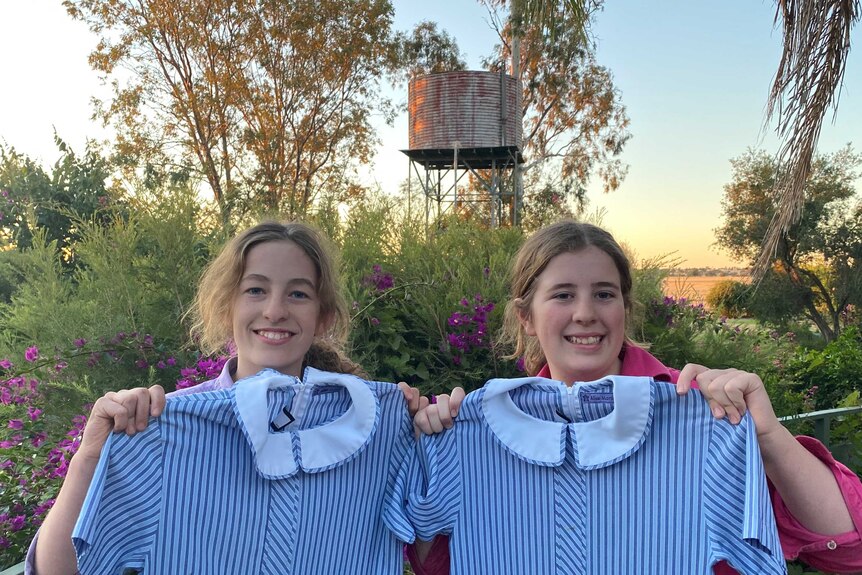 Isobel and Alice hold up their school uniforms.