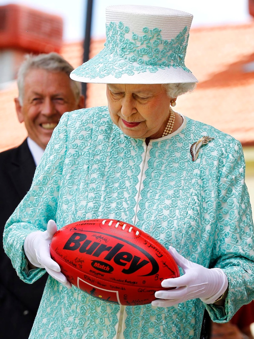 The Queen looks at an Australian Rules football she received while at Clontarf Aboriginal College