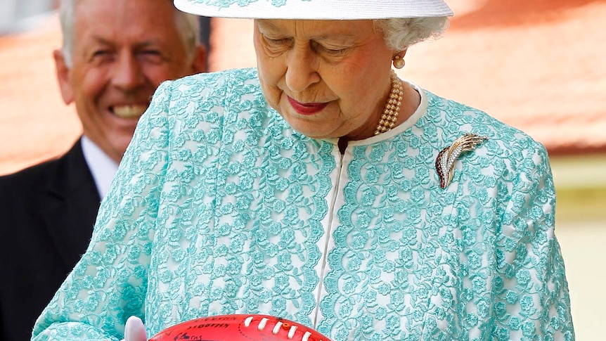 The Queen looks at an Australian Rules football she received while at Clontarf Aboriginal College